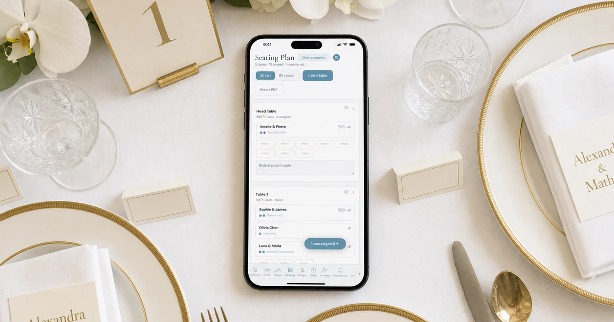 Wedding banquet seating plan Singapore: a phone showing a seating plan app with a head table and Table 1, guests' meals and seats, lying on a white linen round table of ten with gold chargers, place cards and a table number 1