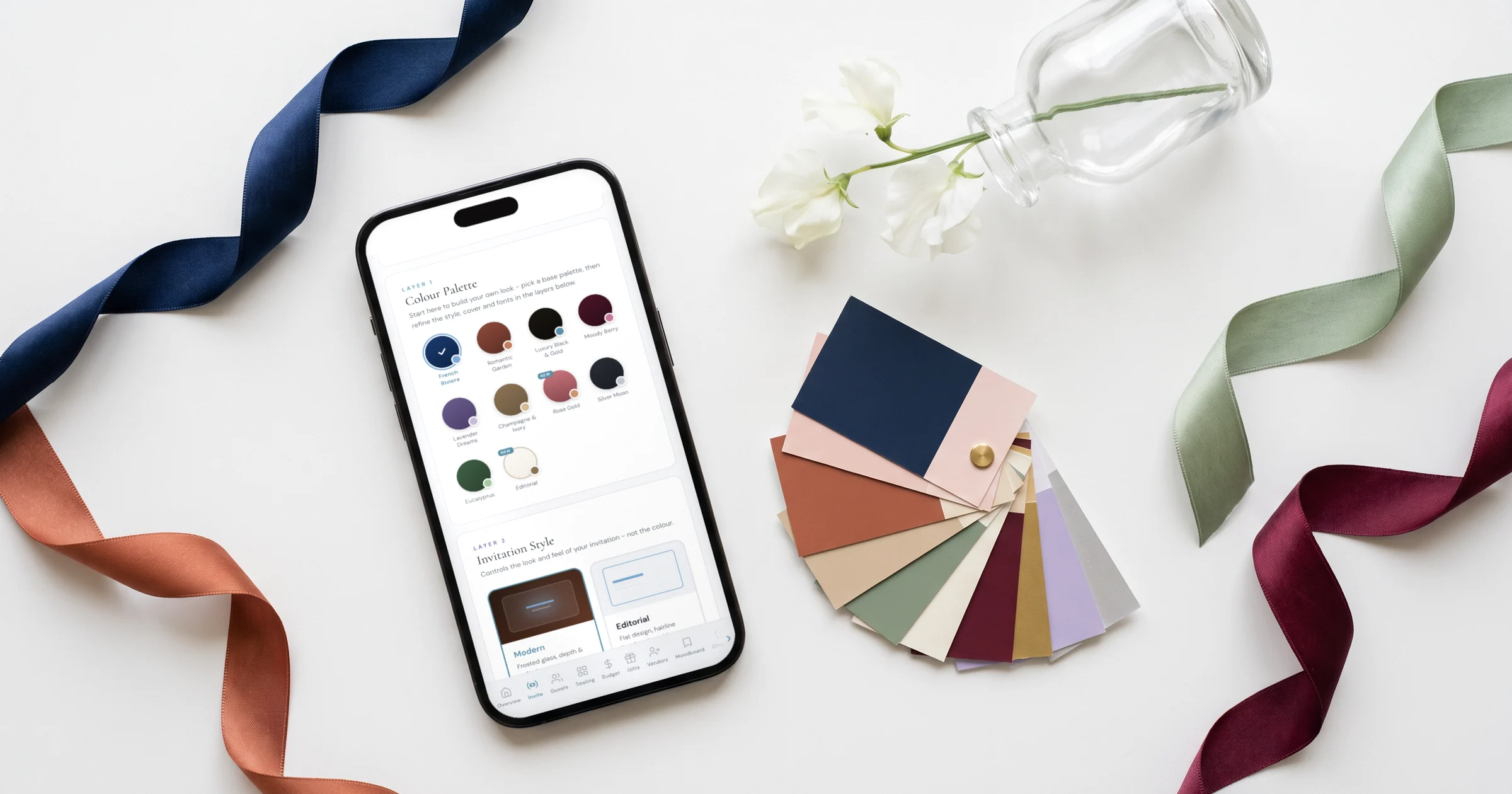 Wedding color palettes 2026: a fan of paint chips and silk ribbons next to a phone showing the invitation colour palette picker