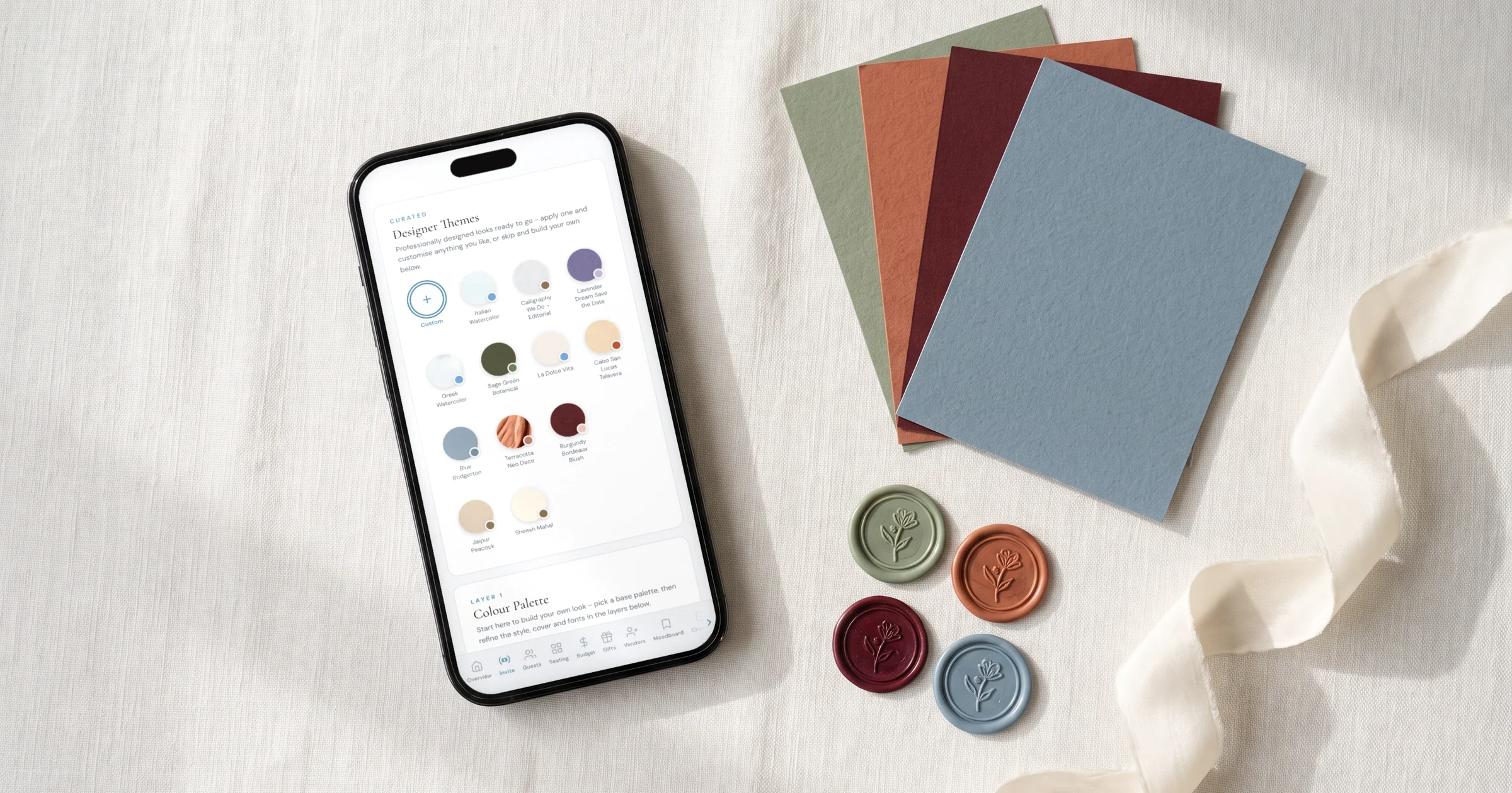 Wedding invitation themes 2026: a phone shows the theme picker beside sage, terracotta, burgundy and dusty blue paper samples and wax seals